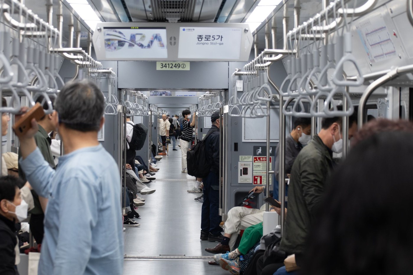 저녁 시간대 지하철 안에서 모바일로 매일경제 경제 뉴스 페이지를 읽고 있는 직장인의 손과 스마트폰 화면을 클로즈업한 장면